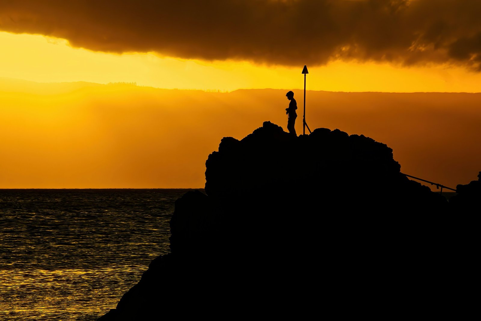 a silhouette of a couple of people on a rock with a sunset in the background with Christ the Redeemer in the background